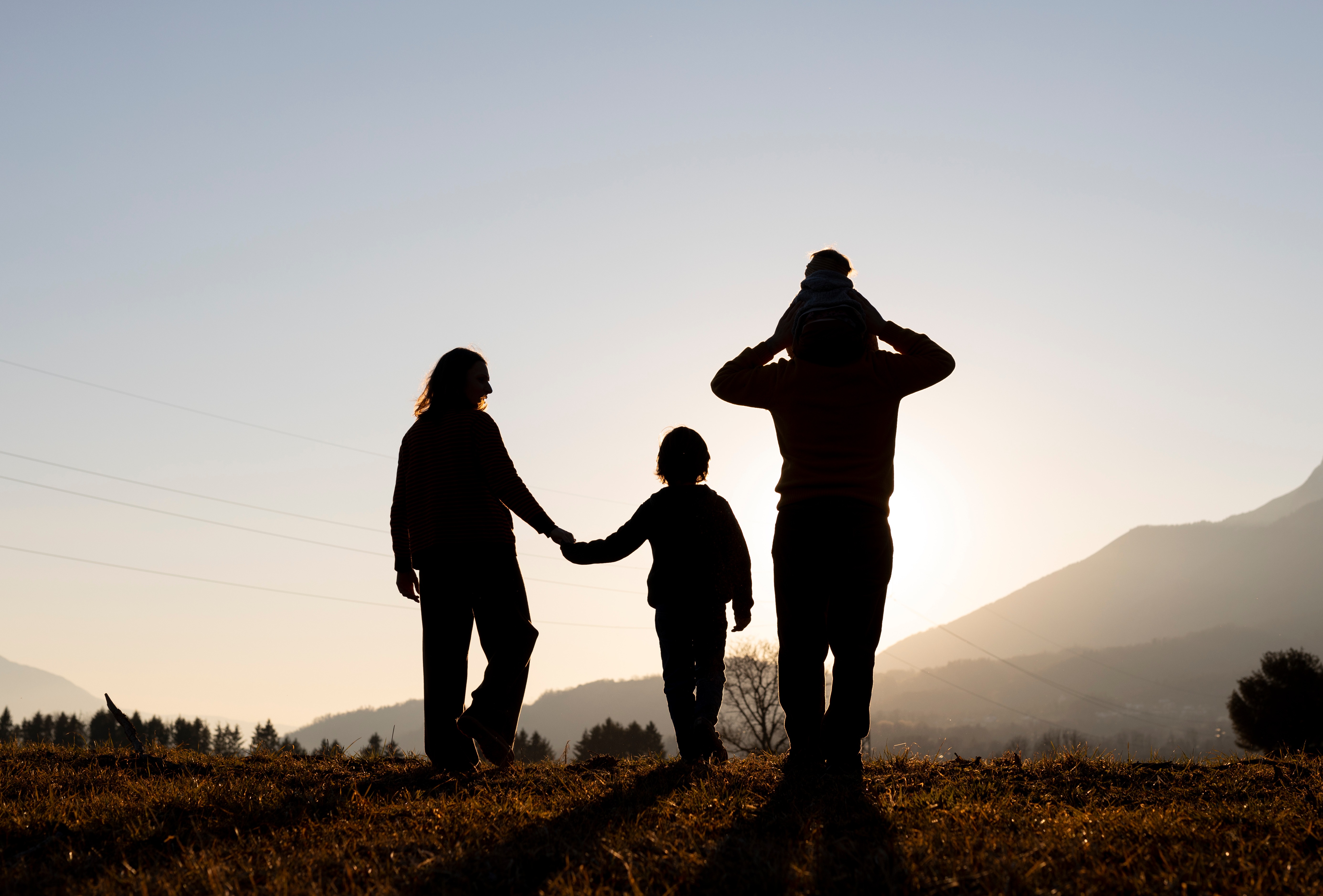 Parents et enfant contemplant un coucher de soleil dans les montagnes des Hautes-Alpes. Cette image symbolise la parentalité, le lien familial, les transitions de vie et l'accompagnement des familles dans le Guillestrois-Queyras.